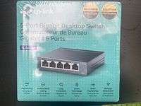Front view of the TP-Link TL-SG105 5-Port Gigabit Desktop Switch packaging showing product image and key features like plug and play, durable metal casing, and green technology.
