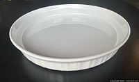 Side angled view showing the vertical fluting around the sides, subtle rimmed edge, and glossy white finish of the ceramic casserole dish.