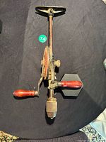 Full view of antique extending shoulder brace hand drill with red wooden handles, metal frame, and black shoulder rest.