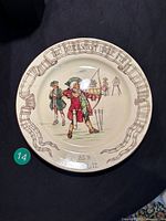 Full view of the antique Royal Doulton rack plate showing the archery scene and ribbon banner title on the rim.