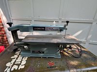 Side view of the Delta 15-inch scroll saw showing the overall construction, bluish gray paint, and cast iron base.