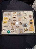 Photo of military collectibles laid out inside glass top display case showing badges, patches, and pins from different military units and ranks