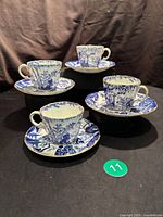 Four Royal Crown Derby blue and white Mikado pattern cups and matching saucers displayed on black background.