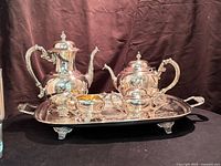 Full view of the entire tea and coffee service on the tray showing all pieces together against a dark cloth backdrop.