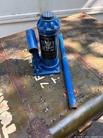 Blue bottle hydraulic jack with pump handle attached, showing operational lever and instructional label.