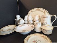 All pieces of a 12 place setting floral pattern dinnerware set including plates, bowls, cups, saucers, and serving pieces arranged with visible floral and gold trim decoration.