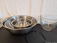 Set of four stainless steel nesting bowls with one glass measuring bowl placed beside them