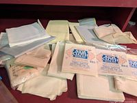 Various folded pieces of Aida cloth fabric in white, cream, and pale yellow colors laid out on a surface with some packages visible.