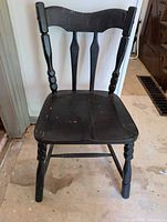 Front view of the antique black wooden chair showing the seat and turned front legs