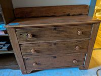 Front view of the antique wooden dresser showing three drawers and curved backboard.