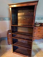Full front view of the tall antique wooden shelving unit with four shelves visible, showing dark wood with wear.