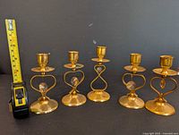 Six brass candle holders arranged in a row with measuring tape showing height.