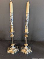 Pair of metal candle holders each with a patterned candle placed inside, shown against a black background.