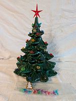 Full ceramic Christmas tree with red star topper and multiple clip-on ornaments attached, along with some replacement ornaments displayed at base.