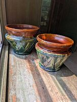 Two ceramic flower pots on a wooden surface in natural light from a window.