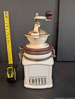 Front and side view of the vintage manual coffee mill showing ceramic base labeled 'COFFEE' and metal grinding mechanism with wooden knob.