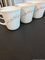 Close-up view of four white Corelle mugs with pink floral design on a black surface.