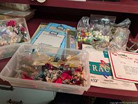 Photo of plastic bins and bags containing various craft supplies including floral picks, beads, ribbons, and packs of Gallery Glass Styrene Blanks and tracing paper.
