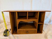 Front view of the wooden desk organizer showing the multiple compartments and drawer with metal knob. Tape measure shows height around 12 inches.