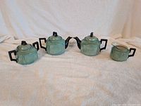 Full set of green lusterware tea set showing two teapots, sugar bowl and creamer on white fabric background.