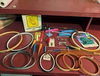 Full lot overview showing all items including hoops, punch needles, cone winder, yarn threaders, and tools on a shelf