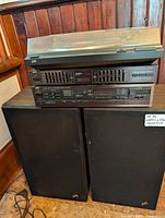 Stereo system components stacked including turntable with plastic cover, amplifier, and equalizer, placed on black speakers with JVC logo.
