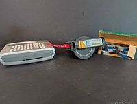 Photo showing grey Dymo label maker with red label tape installed, black label tape cartridge, and box of blank label rolls.