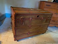 Large wooden trunk with metal corner reinforcements, latches, and circular metal detail on front.