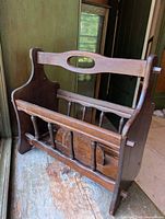 Front angled view of the wooden magazine rack showing carved handle and slatted front design.