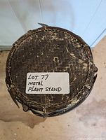 Top-down view of metal plant stand showing textured circular surface and a label stating 'Lot 77 Metal Plant Stand'