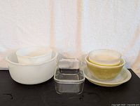 Mixing bowls in white and yellow, glass loaf pan, and other baking items arranged for overview.