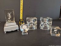 All glass items visible, including two square candle holders, glass clock, etched glass blocks with fairy and fish designs, tape measure for scale