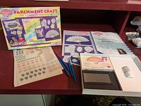 Parchment craft set laid out on table showing box, stencil sheets, pens, embossing tool, and booklet.