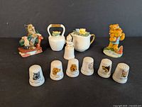 First photo shows seven animal-themed porcelain thimbles arranged in front with four small porcelain figurines behind them on a black background.