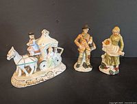 Porcelain man, woman with child, and man standing; horse and carriage figurines on display against black background