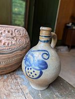 Photo of a small beige jug with blue painted designs, narrow neck and handle.