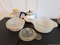 Photo showing three Pyrex bowls with lids, a Corning Ware coffee pot with blue flower design, a small yellow-handled French press juicer, and a glass citrus juicer.