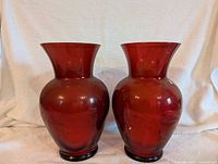 Photo showing both red glass vases side by side on a white cloth background.