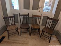 Front view of four vintage wooden chairs showing paint stripping on two chairs and worn paint on others.