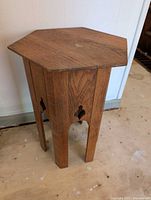 Front and side views of small oak hexagonal side table on a light floor against a white wall.