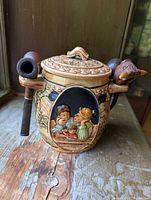 Front view of ceramic pipe holder featuring colorful relief depicting a family scene and three wooden smoking pipes held on the sides.