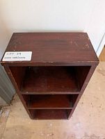 Front view of dark brown solid wood shelving unit with three open shelves, showing wear and scratches.