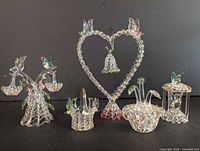 Photo showing six clear spun glass figurines on a black background: a heart-shaped spinning ornament with a hanging bell and birds, two sets of birds perched on floral bases, and two small glass baskets with bird designs.