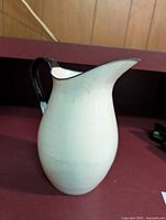Front angle of white ceramic Swiss pitcher with black handle on red surface