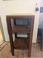 Front view of wooden 3-shelf table showing top surface and two lower shelves with four legs visible.