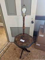 Front view showing the wooden table lamp with light bulb on octagonal maple table with floral painted inlay.