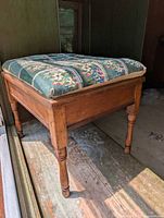 Side view showing the wooden legs and frame of the foot stool and the floral green tapestry cushion.