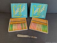 Two open boxes each containing 10 colorful Little Zock tiny forks with original box lids behind them, plus the Boy Scout letter opener/cutter laid below