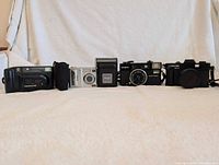 Front view lineup of all five cameras showing the relative size and design of Minolta, Kodak, Minox, Concord, and another compact camera.