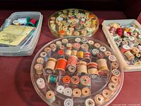 Overview of multiple plastic containers with assorted wooden and plastic thread spools in various colors.